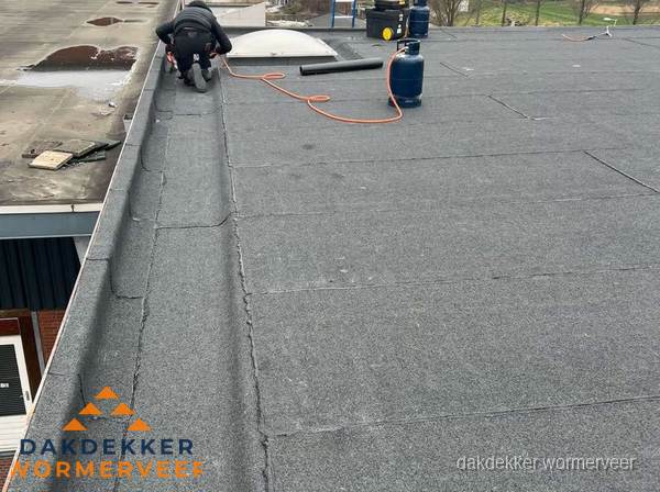Dakdekker repareert bitumen dakbedekking op groot plat dak in Wormerveer