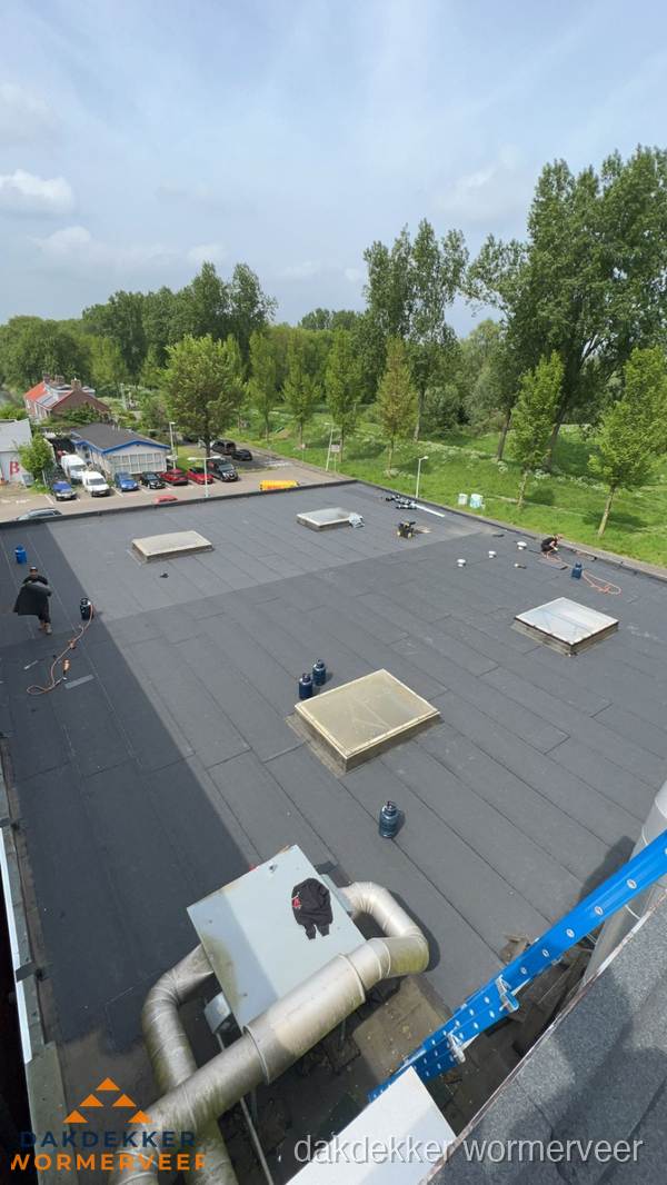 Dakdekker aan het werk op groot plat dak met bitumen in Wormerveer